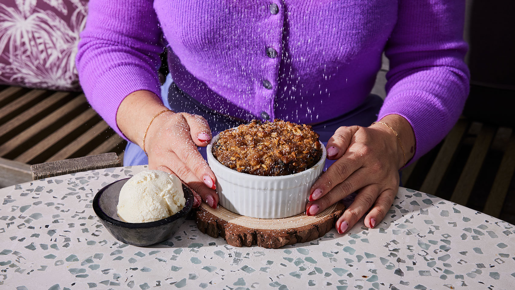 Woman in a purple sweater holding a streusel dish next to a bow of ice cream