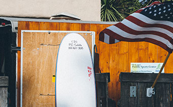 surfboard leaning against a wood fence and an american flag