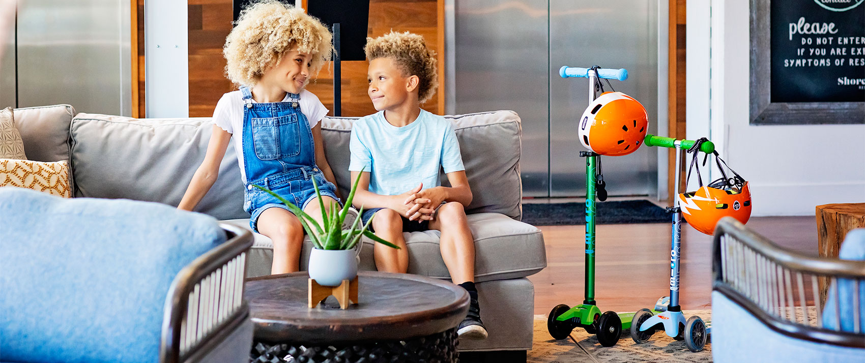 two kids on couch sitting next to two Micro Kickboard Scooters